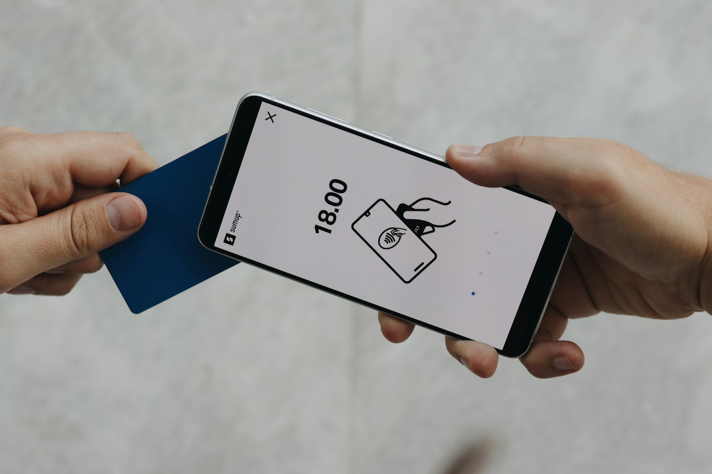 Hände tätigen eine kontaktlose Zahlung mit einem Handy und einer Karte.