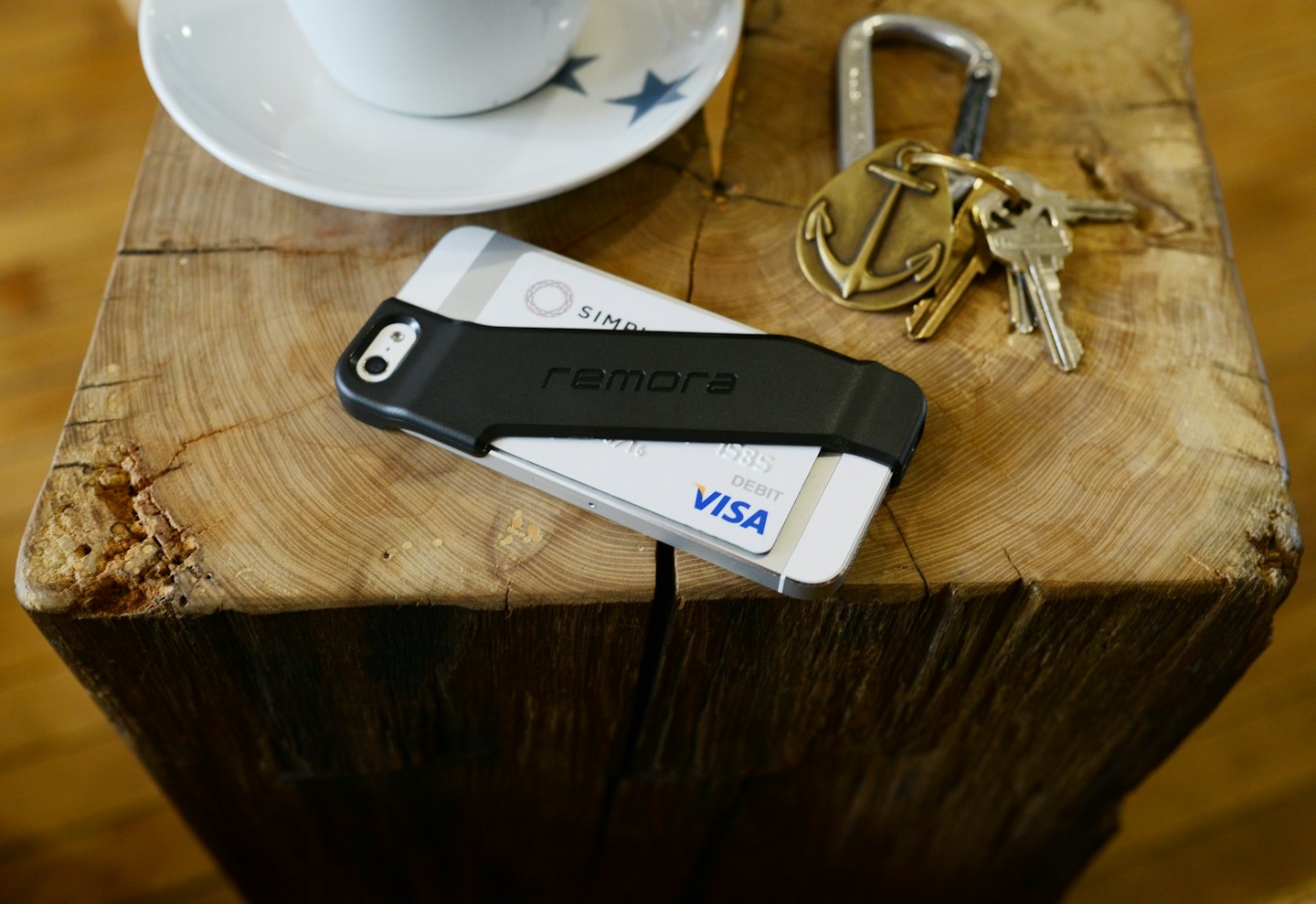 Smartphone mit Kartenhalter liegt neben Kaffee und Schlüsseln auf Holz.
