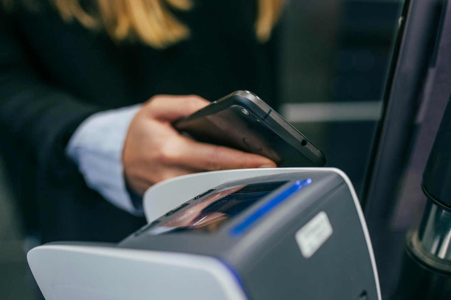 Hand hält Smartphone über kontaktloses Bezahlterminal.
